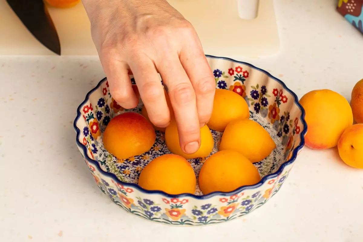 На дно формы для выпечки насыпьте сахар, положите абрикосы