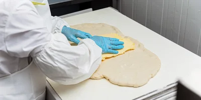 В пласт теста укладывают масло, заворачивают его, а затем прокатывают