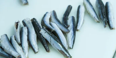 Обезглавленную хамсу помещают в баночки, заливают маслом и  добавляют сушёные пряности — петрушку, паприку и укроп