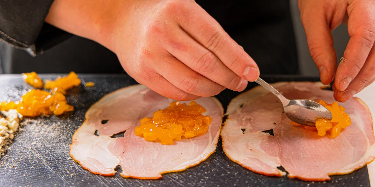 Выложите на ломтики окорока измельчённую хурму и сыр