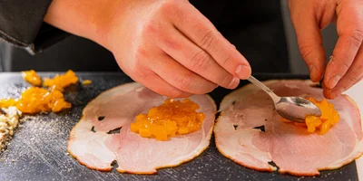 Выложите на ломтики окорока измельчённую хурму и сыр