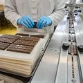 Сотрудники вручную выкладывают шоколадные плитки на упаковочный стол