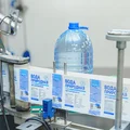 Наполненная водой бутылка поступает по транспортёру на этикетировку