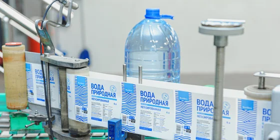 Наполненная водой бутылка поступает по транспортёру на этикетировку